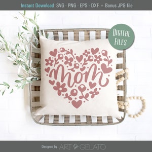 K&ouml;nnte beinhalten: Ein wei&szlig;es Kissen mit einem roten Herzdesign, das das Wort "mom" zeigt, umgeben von Blumen und Herzen. Das Kissen liegt in einer Holzschale.
