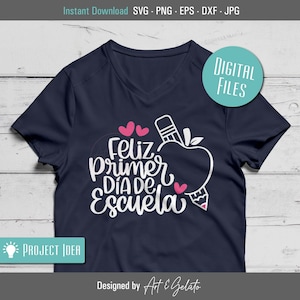 May include: A navy blue t-shirt with a white graphic design that says "Feliz Primer Dia de Escuela" with a pink apple and pencil design.