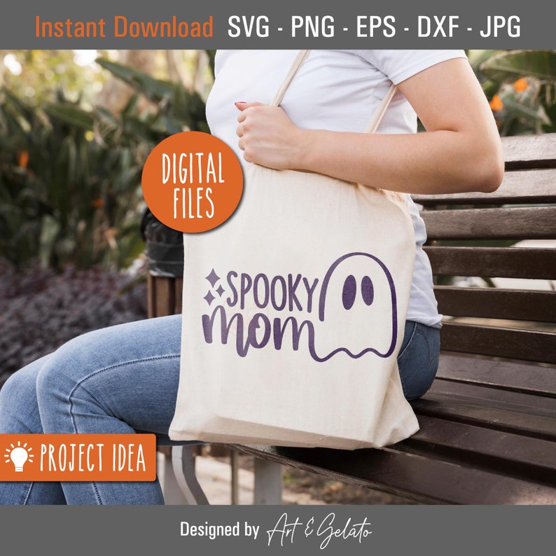 May include: A white tote bag with a purple ghost and the text "SPOOKY mom" on it. The bag is being held by a person wearing blue jeans and a white shirt.