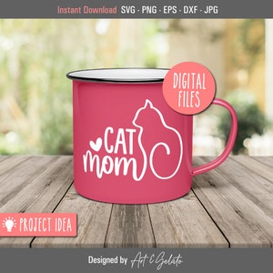 May include: A pink enamel mug with a white silhouette of a cat and the text "CAT mom" with a heart. The mug is on a wooden surface.
