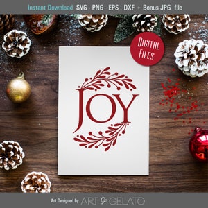 Op de afbeelding: Een witte kaart met een rood kransontwerp en het woord "JOY" in het midden. De kaart ligt op een houten oppervlak met dennenappels en rode ornamenten.