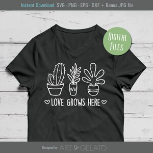 May include: A black t-shirt with a white design of three potted plants and the text "LOVE GROWS HERE" in a heart-shaped frame. The design is in a simple, hand-drawn style.