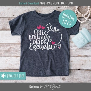 May include: A dark gray t-shirt with a white graphic design that says "Feliz Primer Dia de Escuela" with a red apple and pencil. The design is on a dark gray t-shirt.