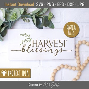 May include: A white wooden sign with the text "HARVEST blessings" in brown lettering. Green leafy sprigs are above the text. The sign is on a white brick background with a wooden bead garland.