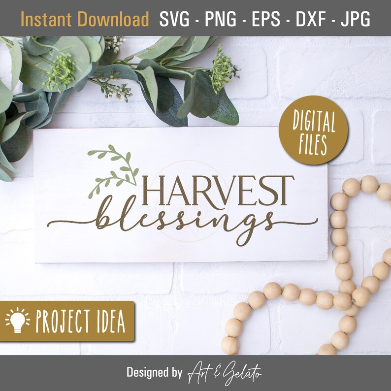 May include: A white wooden sign with the text "HARVEST blessings" in brown lettering. Green leafy sprigs are above the text. The sign is on a white brick background with a wooden bead garland.