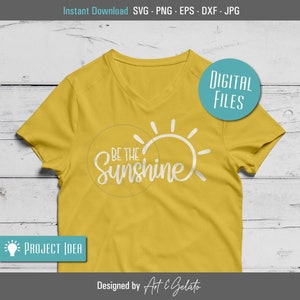 May include: A yellow t-shirt with a white sun graphic and the text "Be the Sunshine" on the front. The shirt is on a wooden surface.