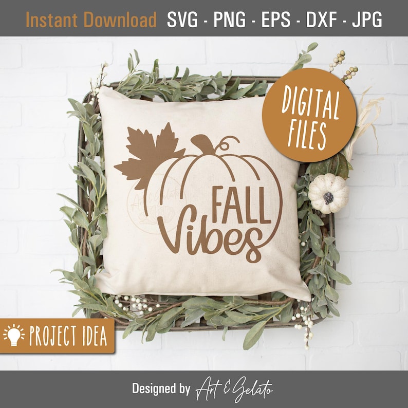 May include: A white pillow with a brown pumpkin and leaf design and the text "FALL Vibes". The pillow is sitting in a woven basket with greenery.