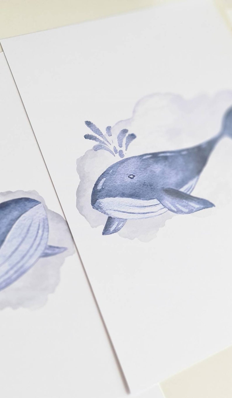 May include: Watercolor illustration of a blue whale with a water spout, set against a soft gray cloud. The whale is depicted in shades of blue, with a detailed fin and tail. The artwork is on a white background.