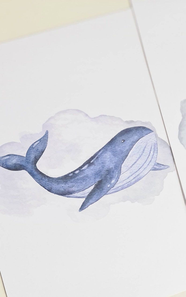 May include: Watercolor illustration of a blue whale swimming in a lavender cloud. The whale has a detailed design with a white belly and a curved tail. The artwork is on a white background.