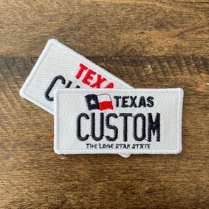 May include: Two white embroidered patches with black and red text. One patch reads "TEXAS CUSTOM" with a Texas flag graphic and "THE LONE STAR STATE" below. The other patch reads "TEXAS" in red.