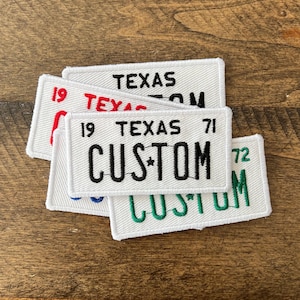 May include: White rectangular patches embroidered with the word "TEXAS" and the word "CUSTOM" in various colors. The patches resemble license plates, with the year "19", "71", and "72" also embroidered.