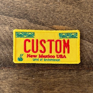May include: Yellow embroidered patch with the word "CUSTOM" in red lettering. The patch also has the text "New Mexico USA Land of Enchantment" in green lettering.