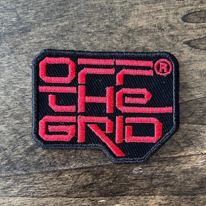 May include: A black fabric patch with red embroidered text that reads "OFF THE GRID" with a registered trademark symbol.