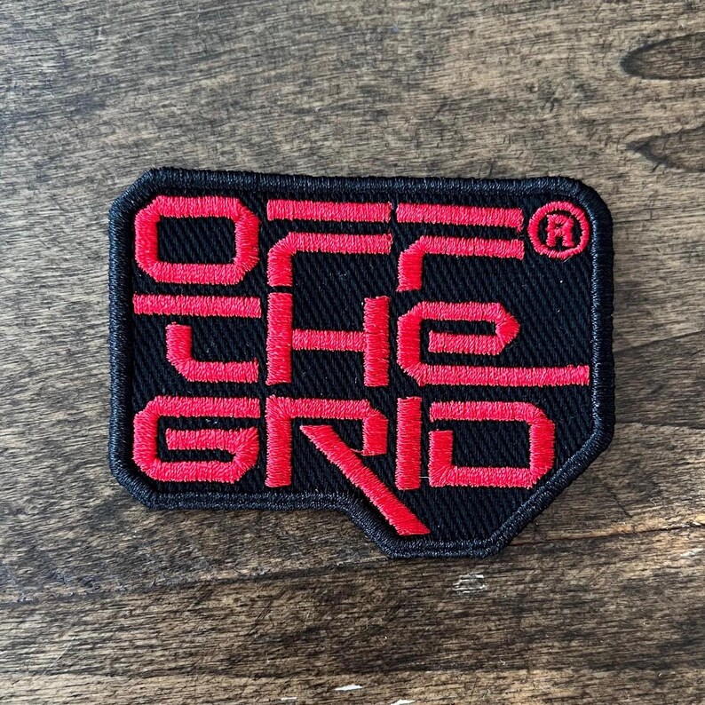 May include: A black fabric patch with red embroidered text that reads "OFF THE GRID" with a registered trademark symbol.