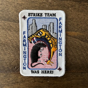 May include: White embroidered patch with a yellow snake biting a black rat. The patch has blue text that reads "Strike Team Farmington Was Here!"