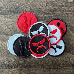 May include: A set of eight embroidered iron-on patches featuring a cartoon face with sunglasses and a mustache. The patches are in red, black, and white.