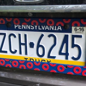 May include: A blue and red license plate with a donut pattern border. The plate reads "PENNSYLVANIA" and "ZCH-6245" with a truck sticker. The plate also has a small sticker that reads "6-16 0085917".