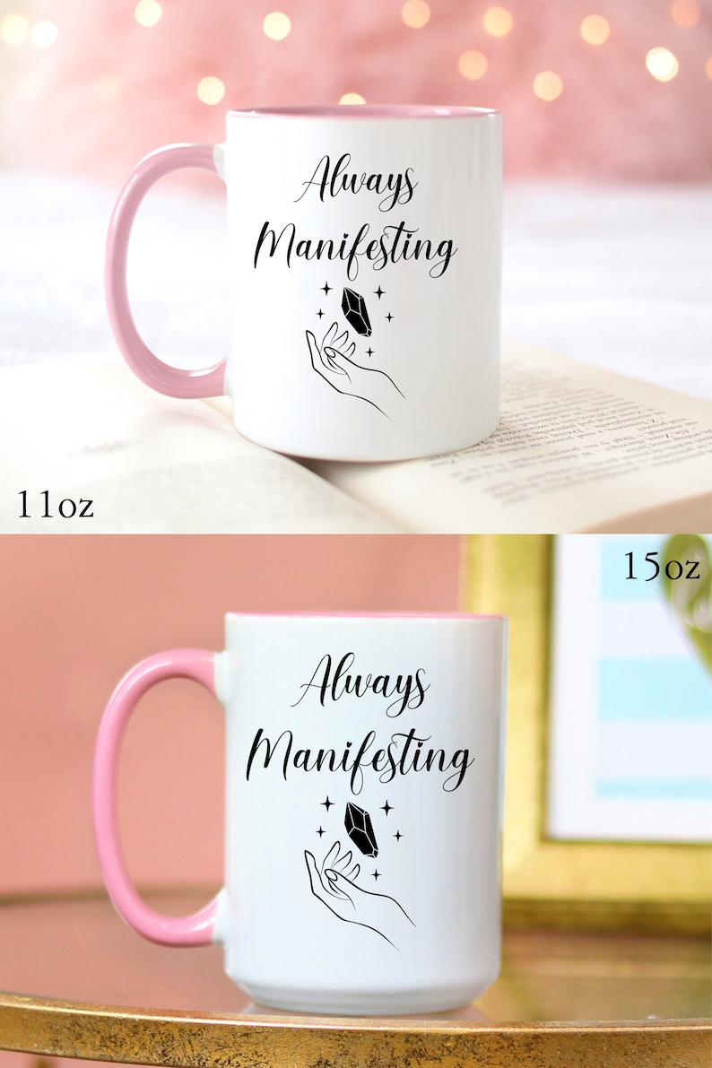 May include: White ceramic mug with a pink rim and handle. The mug has a black design of a hand holding a crystal with the text "Always Manifesting".