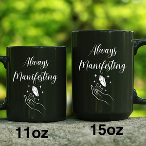 May include: Two black ceramic mugs with white text and a crystal design. The text on the mugs reads "Always Manifesting". The mug on the left is 11 oz and the mug on the right is 15 oz.