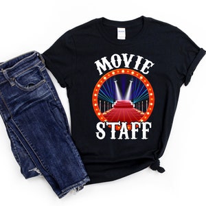 May include: Black t-shirt with white text that reads "Movie Staff" and a red carpet with spotlights graphic.