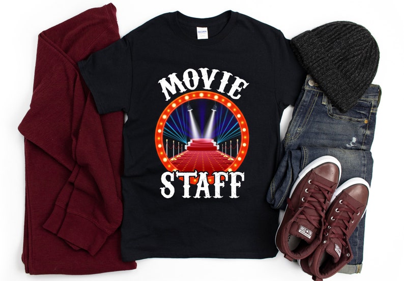 May include: Black t-shirt with white text that reads "MOVIE STAFF" and a graphic of a red carpet with spotlights.