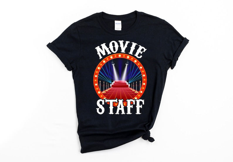 May include: Black t-shirt with a white circle graphic featuring a red carpet, spotlights, and the text "MOVIE STAFF".