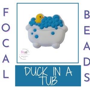 May include: A white bathtub-shaped bead with blue bubbles and a yellow duck. The text "DUCK IN A TUB" is displayed in a blue rectangle. The image is framed with the words "FOCAL BEADS".