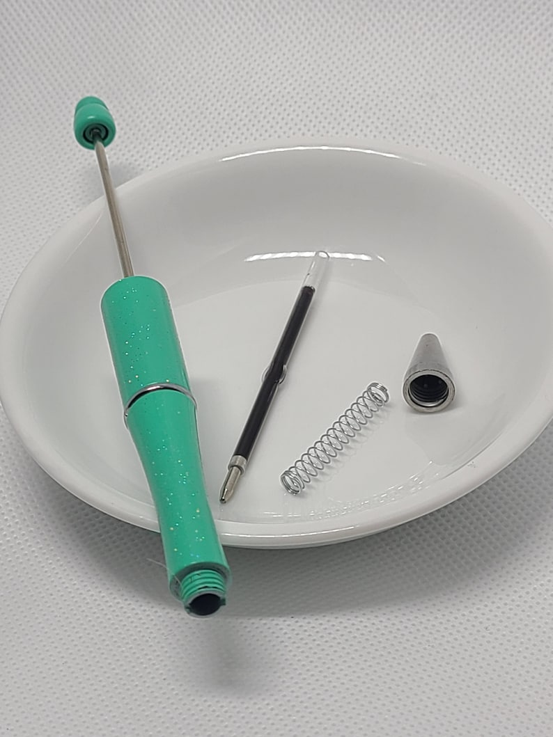 May include: A disassembled turquoise glitter pen with a silver metal tip, a metal spring, and a black ink refill. The pen body features a sparkly finish and a silver center band. The components are laid out separately to show the internal parts.