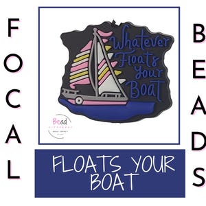 May include: A black, blue, and white charm with a sailboat design. The charm has a pink and yellow sail and the phrase "Whatever Floats Your Boat" in white script. The words "Focal Beads" and "Floats Your Boat" are also visible.