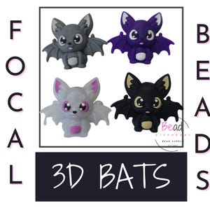 Könnte beinhalten: Vier 3D-Fledermaus-Anhänger in verschiedenen Farben: Grau, Weiß, Lila und Schwarz. Jede Fledermaus hat große Augen und einen süßen Ausdruck. Die Fledermäuse sind mit "3D Bats" und "Focal Beads" beschriftet.