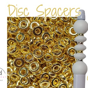 May include: Gold disc spacers, 6mm in size. A close-up image shows a pile of gold-colored metal spacers. The spacers are round with a hole in the center. The image also shows a white and gold-colored spacer on a stick.