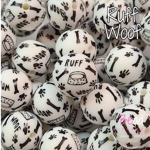 May include: A close-up of a pile of white silicone teething beads with black paw prints, bones, and the words "Woof" and "Ruff" printed on them.