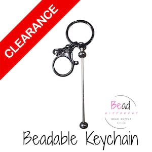 May include: A black beadable keychain with a lobster clasp, a key ring, and a long, thin metal rod with a bead at each end. The word "CLEARANCE" is in white text on a red diagonal banner. The text "Beadable Keychain" is below the keychain.