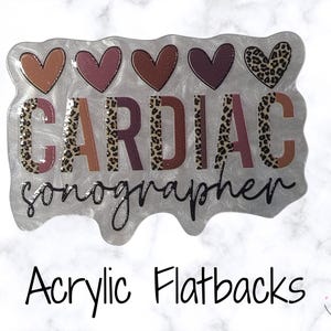 May include: An acrylic flatback with the text "CARDIAC sonographer" in a mix of colours and leopard print. Above the text are five heart shapes in shades of orange, pink, and leopard print. The flatback has a silver, marbled background.