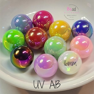 Puede incluir: Una colecci&oacute;n de cuentas iridiscentes UV AB en varios colores, incluyendo rosa, verde, amarillo y morado, dispuestas sobre un plato blanco. Cada cuenta mide aproximadamente 1,6 cm de di&aacute;metro. El texto "Bead" y "UV AB" es visible.