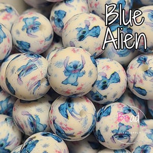 May include: A close-up of a pile of white silicone beads with a blue alien character print. The beads are approximately 2 cm in diameter and have a matte finish. The text "Blue Alien" is visible in the image.