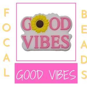 以下が含まれることがあります： 白いチャームにピンクの「GOOD VIBES」のメッセージと黄色のひまわりが描かれています。チャームは靴やバッグ用です。