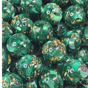 May include: A collection of round acrylic beads featuring a deep green base with embedded gold-colored foil flakes. The word ACRYLIC is printed vertically in black on the left side, and the text Bead Supply is visible on the right.