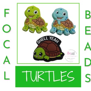 May include: Three turtle charms, one green, one blue, and one brown. The green turtle has a brown shell and the blue turtle has a brown shell. The brown turtle has a brown shell and the words "Shell Yeah" on its shell.