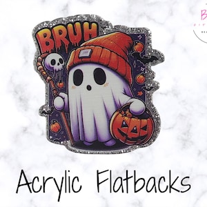 Puede incluir: Un flatback acrílico con temática de Halloween con un fantasma de dibujos animados que lleva un gorro naranja y sostiene una calabaza y un bastón con una calavera. La palabra "BRUH" está encima del fantasma en letras naranjas. El flatback tiene un borde plateado brillante.