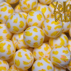 May include: A close-up of a group of white silicone beads with yellow duck illustrations. The beads are arranged in a random pattern and are all the same size. The text "Yellow Duck" is visible in the top right corner of the image.