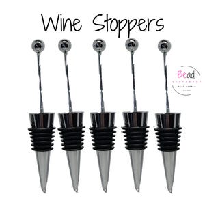 May include: Five silver wine bottle stoppers with black rubber bases. The stoppers have a cone-shaped design with a round ball on top.
