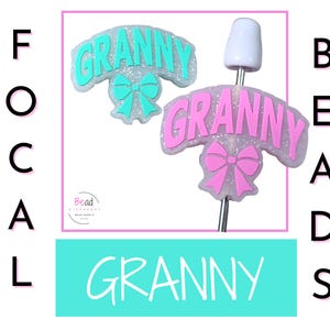 May include: Two focal beads with the word "GRANNY" in aqua and pink, with a bow design. One bead is on a silver pin with a white top. The word "FOCAL" is written vertically on the left, and "BEADS" on the right.