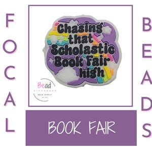 May include: A purple and white cloud-shaped charm with a rainbow design and the text "Chasing that Scholastic Book Fair high".