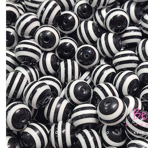 May include: A close-up image of black and white striped acrylic beads. The beads are round and have a glossy finish.