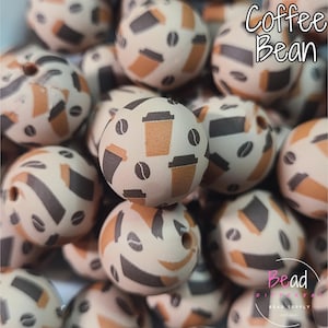 Könnte beinhalten: Nahaufnahme von cremefarbenen Perlen mit Kaffeemotiv. Die Perlen zeigen braune Kaffeetassen, Kaffeebohnen und abstrakte Formen. Der Text "Coffee Bean" befindet sich in der oberen rechten Ecke. Die Perlen sind für die Schmuckherstellung.