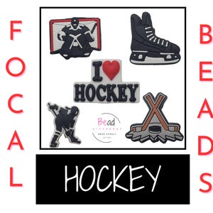 May include: Five hockey-themed shoe charms. The charms include a hockey player, a hockey net, a pair of hockey sticks, a hockey puck, and a charm that says "I love hockey" with a red heart.