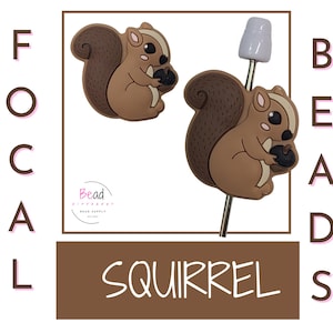 May include: Two brown squirrel focal beads with a white bead on a silver wire. The beads are holding acorns. The text "FOCAL" is on the left and "BEADS" is on the right. The text "SQUIRREL" is in the center.