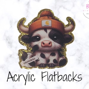 May include: Acrylic flatback featuring a cute black and white cow wearing an orange beanie with a Carhartt logo. The cow has gold glitter edging and a tag that says "ORIGINAL". The image is on a white marble background.