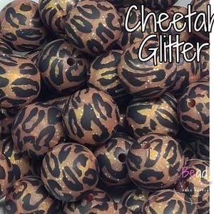 May include: A close-up of a group of brown and black cheetah print silicone beads with gold glitter. The beads are round and have a textured surface. The text "Cheetah Glitter" is visible in the image.